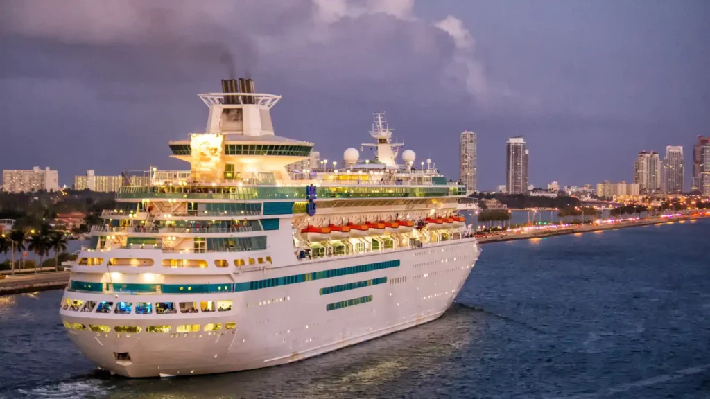 cruise ship sailing near a city shoreline at dusk
